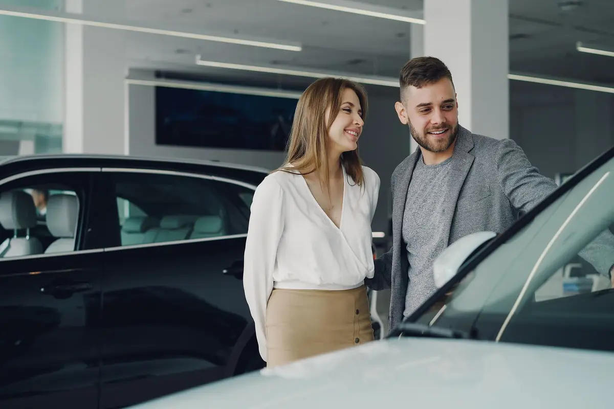 A couple looking over a car with a JE Auto salesperson in the showroom