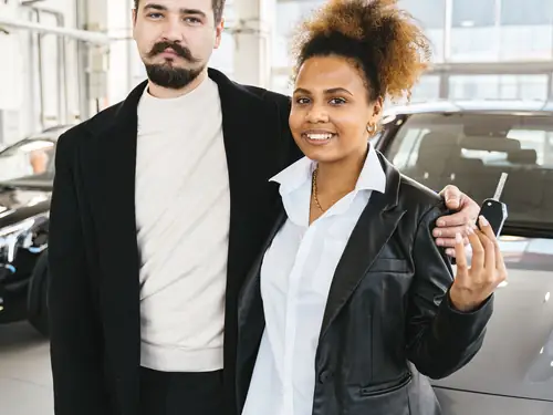 A couple standing beside their newly bought car holding the keys
