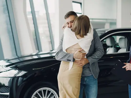 A couple embracing beside their new car in the showroom
