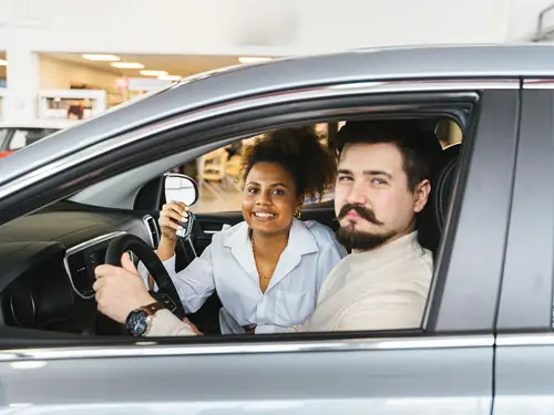 A couple sitting in their new car, the driver holding up the key