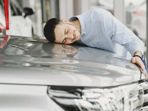 A delighted buyer resting against the bonnet of his new vehicle