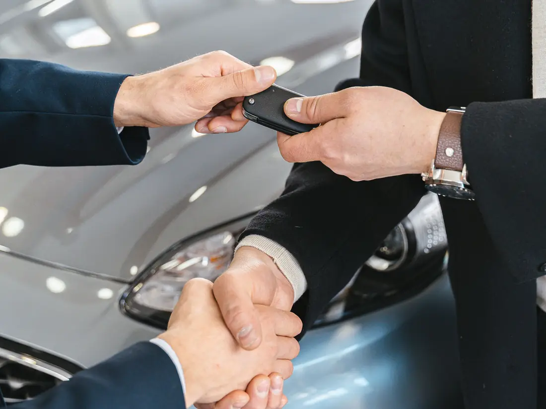 A handshake and car keys changing hands over an open car door