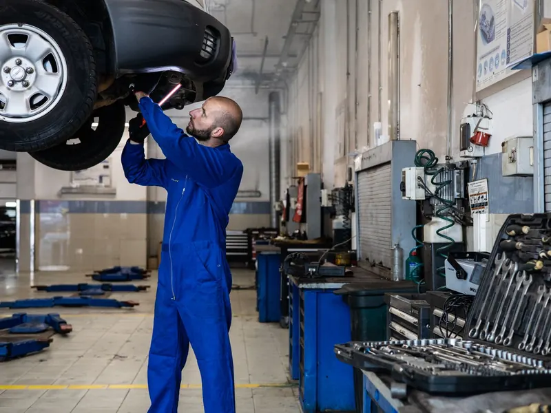 A technician checking the underside and suspension of a raised vehicle